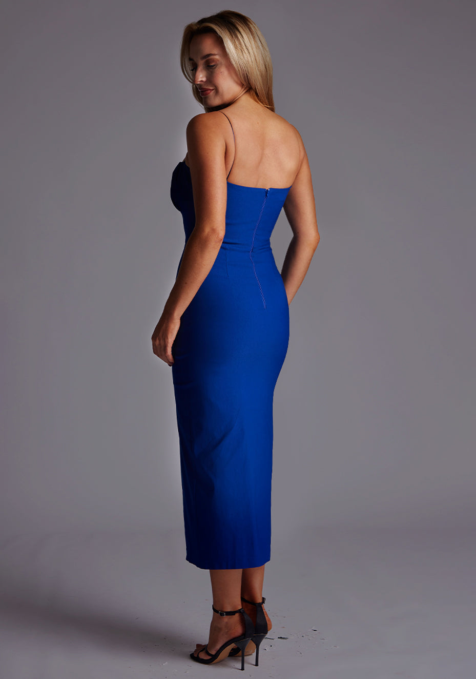 Back quarter image of a model wearing a cobalt midaxi dress with a charming sweetheart neckline with a ruched front design, delicate thin straps and graceful front skirt split. The design featured is the Vesper Alex Cobalt Midaxi Dress