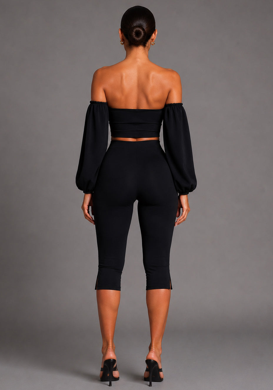 Back image of a model wearing the VSPR Belle Sweetheart Neckline Puff Sleeve Black Top featuring dramatic sleeve detailing, a sleek fitted design, and a polished silhouette. The design paired with Capri Black Cropped Trousers. posed against a grey studio backdrop.