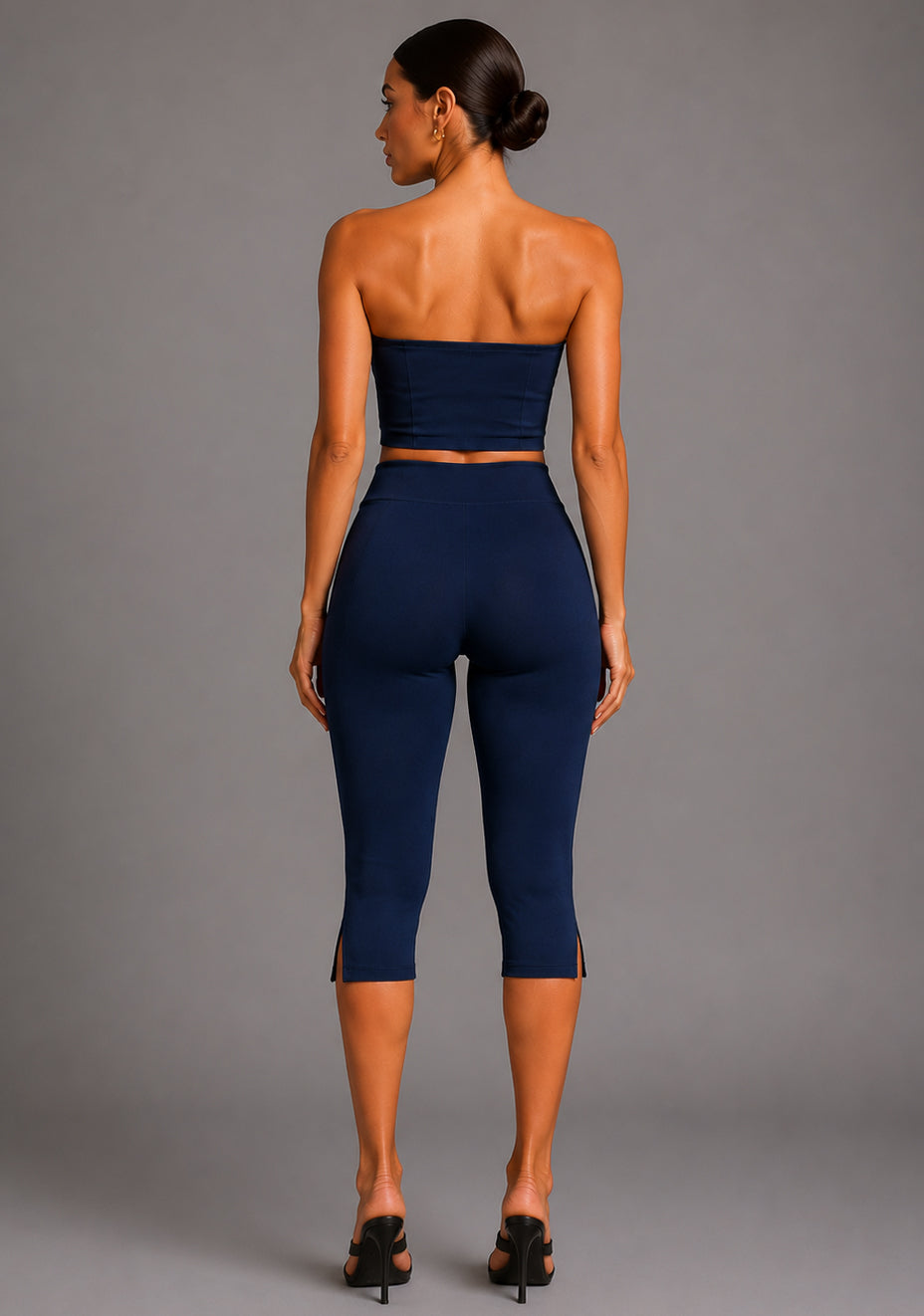 Back image of a model wearing the VSPR Benedetta Strapless Navy Crop Top in navy, featuring a clean strapless back and streamlined tailored fit. The design paired with Capri Cropped Navy Trousers, against a grey studio backdrop.