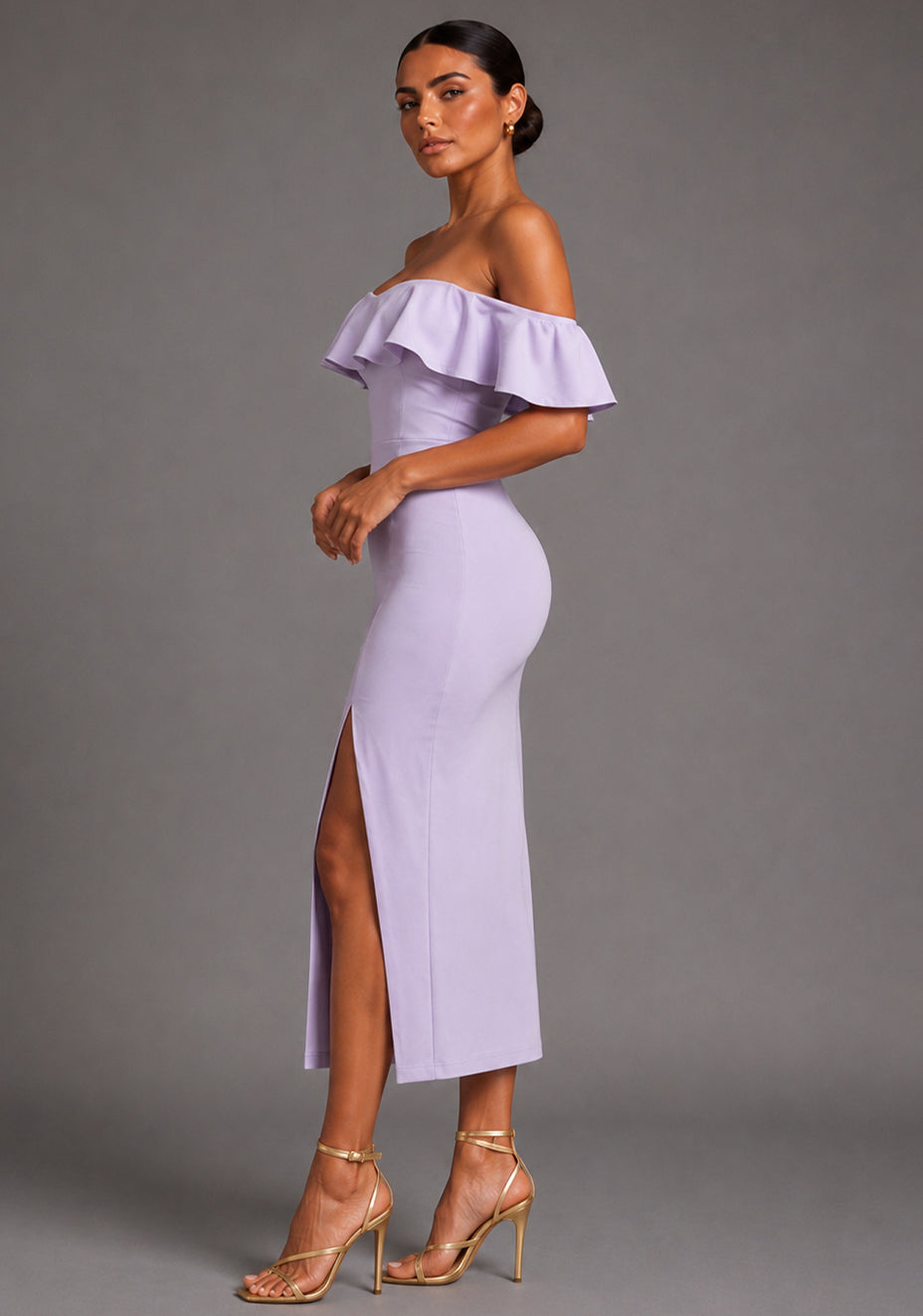 Side front image of a model wearing the VSPR Deirdre Bardot Off-Shoulder Frill Lilac Midaxi Dress highlighting the Bardot neckline, flowing frill accents, flattering fitted silhouette, and front skirt split against a grey studio backdrop.