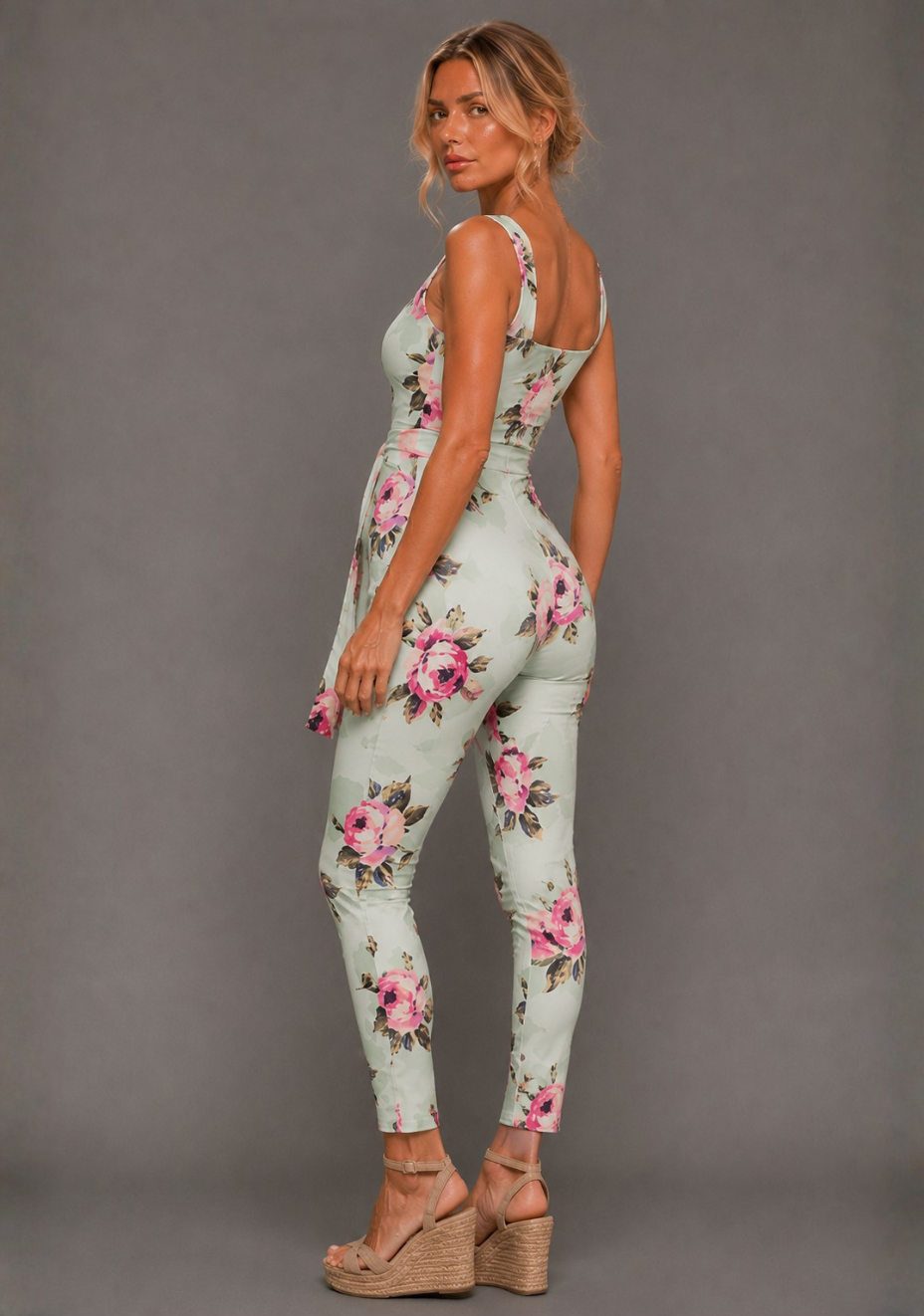 Side back image of a model wearing the VSPR Nala Square Neckline Mint Floral Jumpsuit in Mint Floral, highlighting the waist definition and tapered leg silhouette, standing against a grey studio backdrop