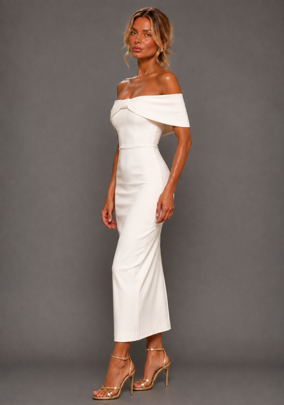 Side front image of a model wearing the VSPR Sarah Bardot Bodycon Ivory Midaxi Dress, highlighting the shoulder-baring neckline and sleek body-contouring silhouette against a grey studio backdrop