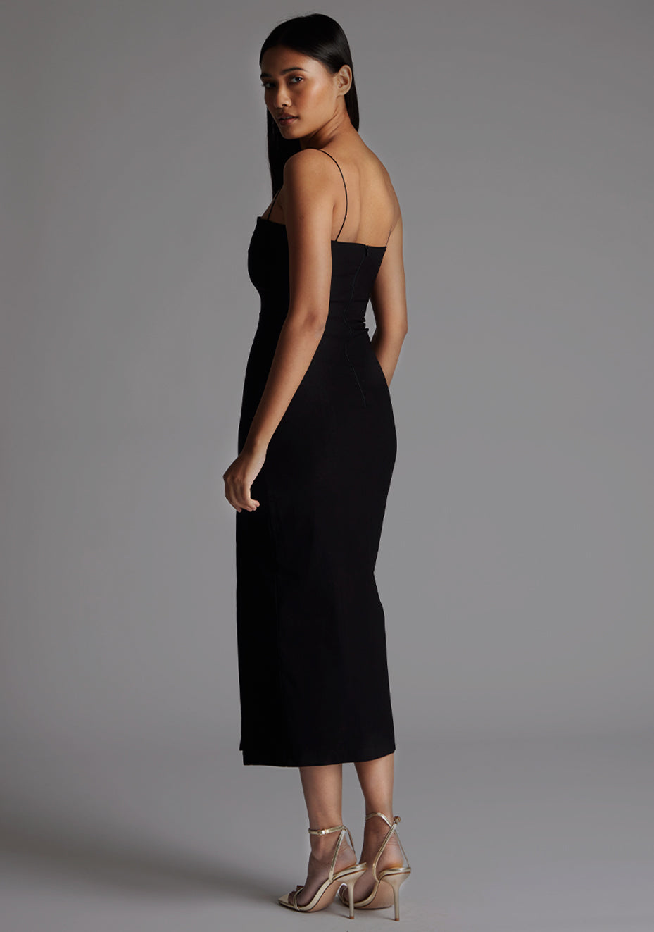 Side back image of a model wearing the Vesper Adeline Cut Out Midaxi Dress in Black revealing the elegant strap placement and smooth, sculpting fabric finish.