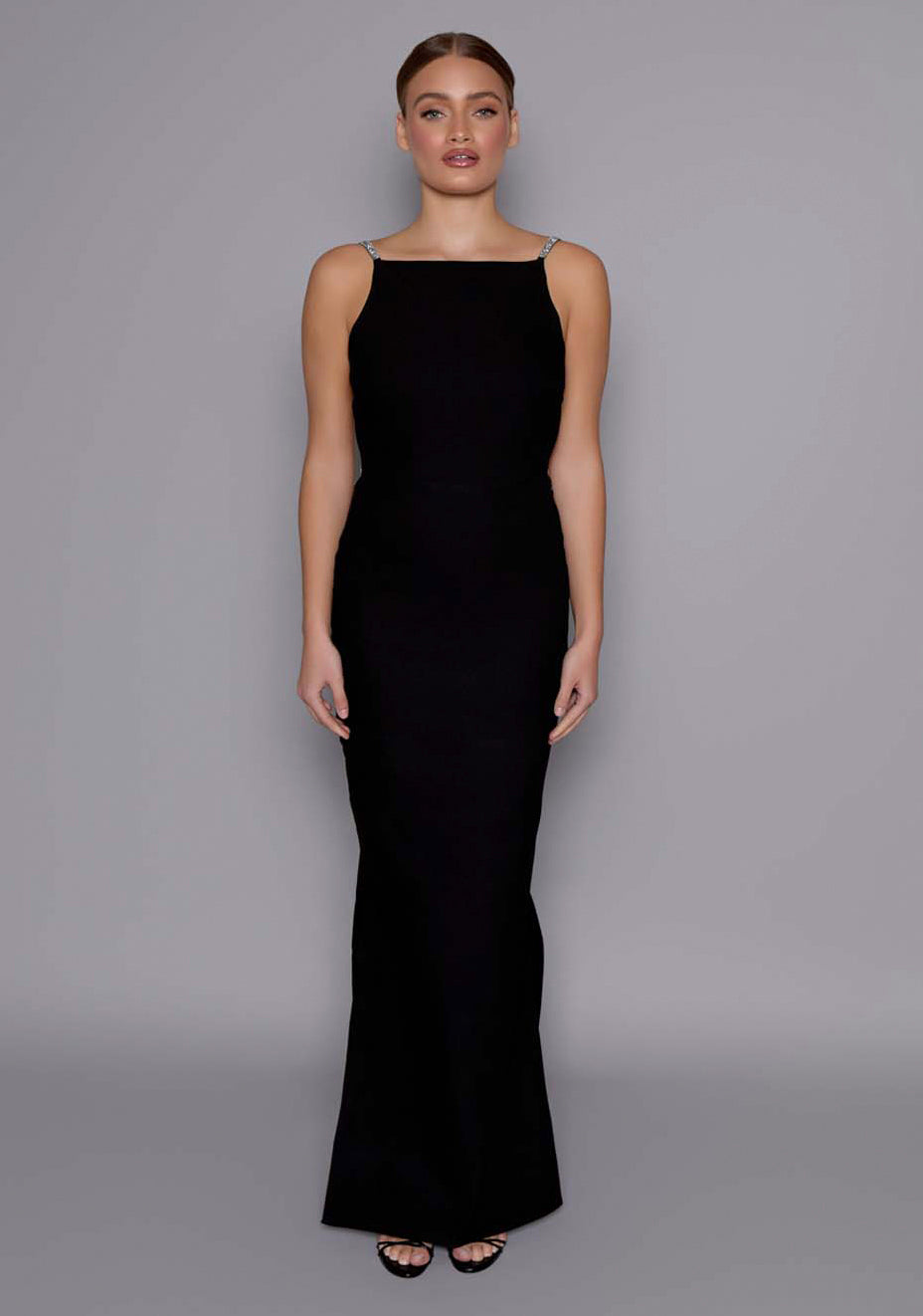 Model wearing the VSPR Alba black maxi dress with a structured square neckline and body-skimming silhouette, standing against a grey studio backdrop