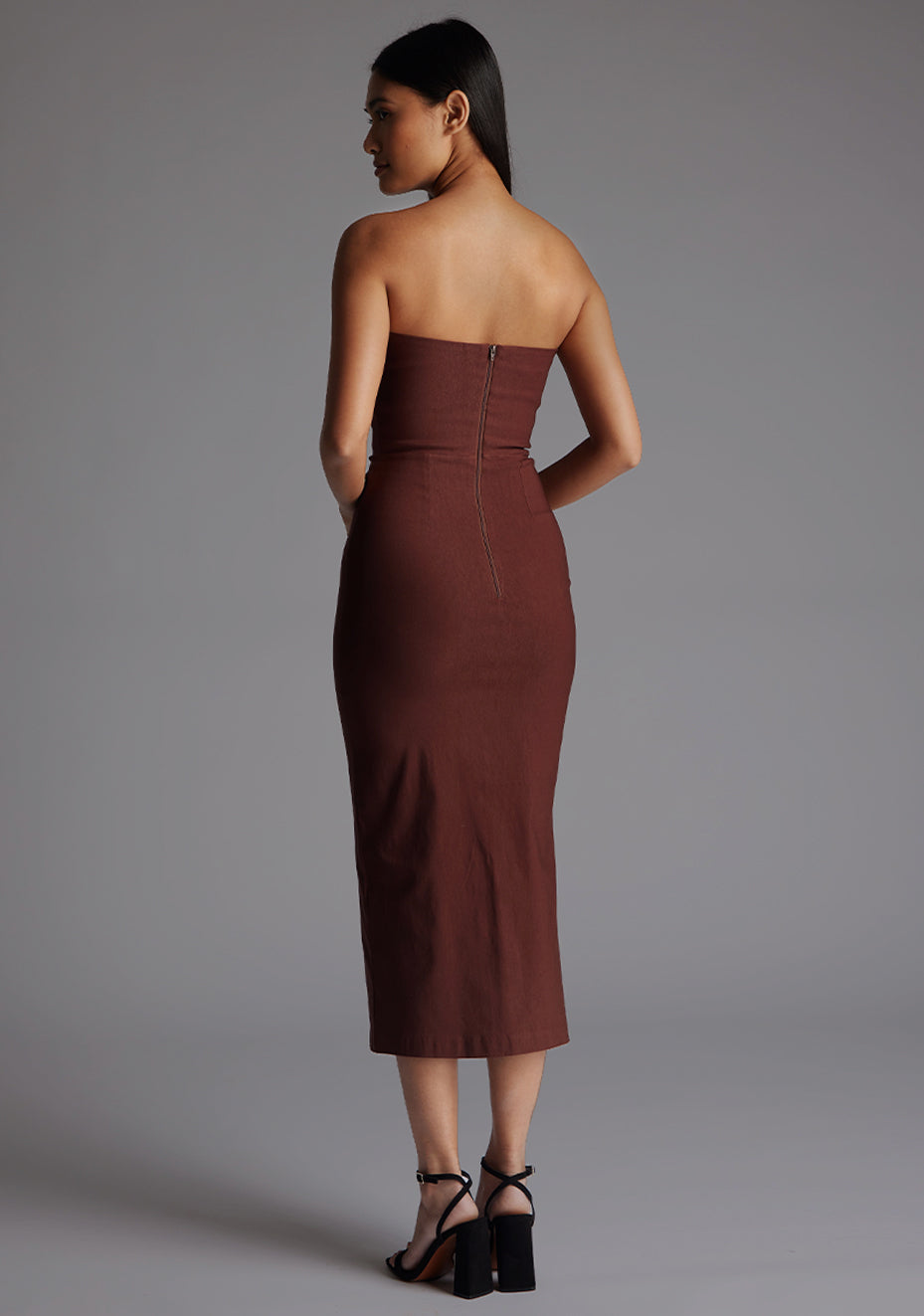 Side back view of a model wearing the Vesper Andorra Strapless Midaxi Dress in Chocolate, showcasing the clean lines of the strapless design and the dress’s sculpted silhouette.