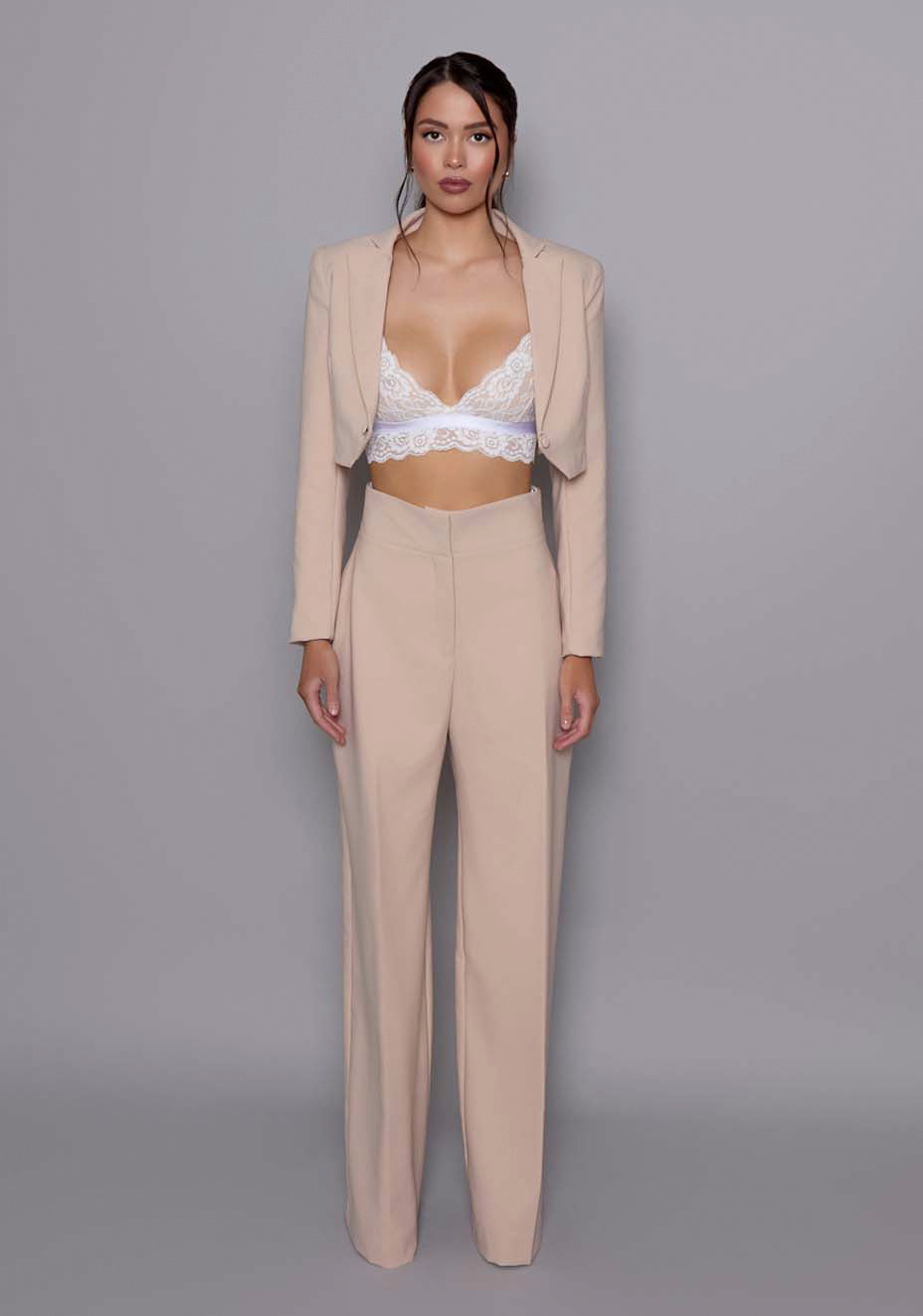 Model wearing the VSPR Aria cropped tailored Jacket in Stone, featuring sharp lapels, sculpted waist, and clean architectural lines, against a neutral gray studio backdrop.