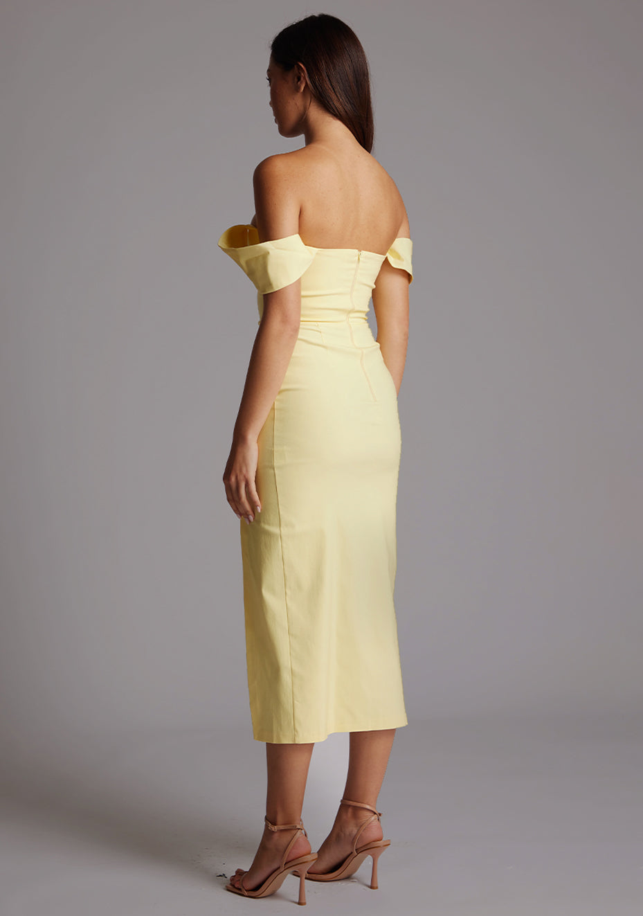Back quarter image of a model wearing a yellow Bardot midaxi dress with a stunning Bardot neckline with armbands and a front skirt split. The design featured is the VSPR Astra Yellow Bardot Midaxi Dress.