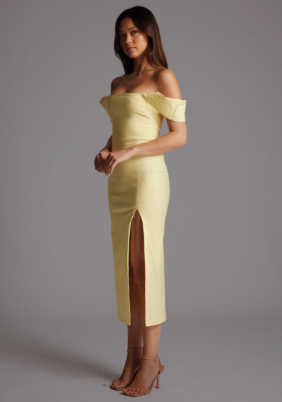 Front quarter image of a model wearing a yellow Bardot midaxi dress with a stunning Bardot neckline, with armbands and a front skirt split. The design featured is the VSPR Astra Yellow Bardot Midaxi Dress.
