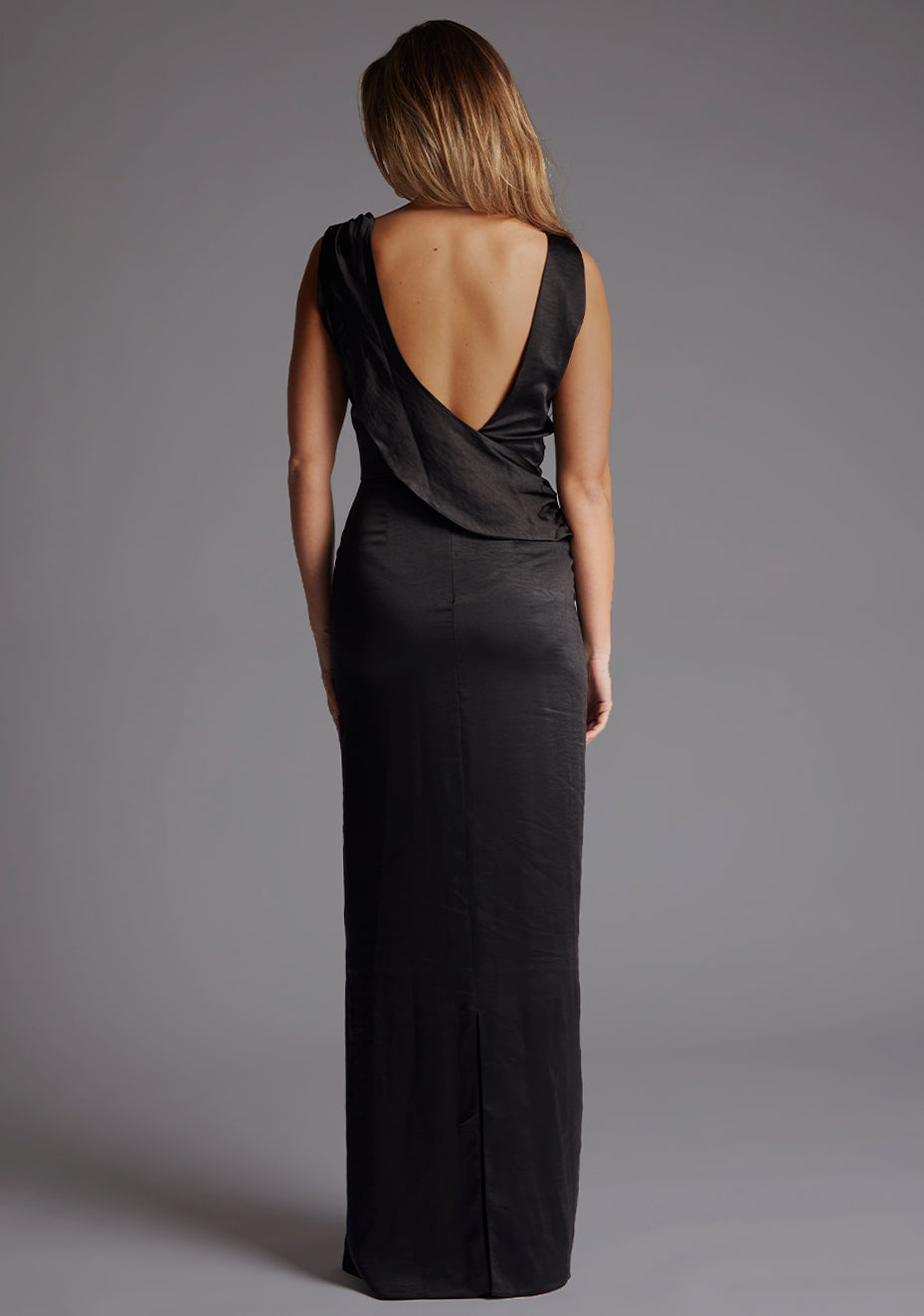 Back image of a model wearing the Vesper Bertie Open Back Satin Maxi Dress in Black, emphasizing its dramatic open-back detail and timeless evening elegance.