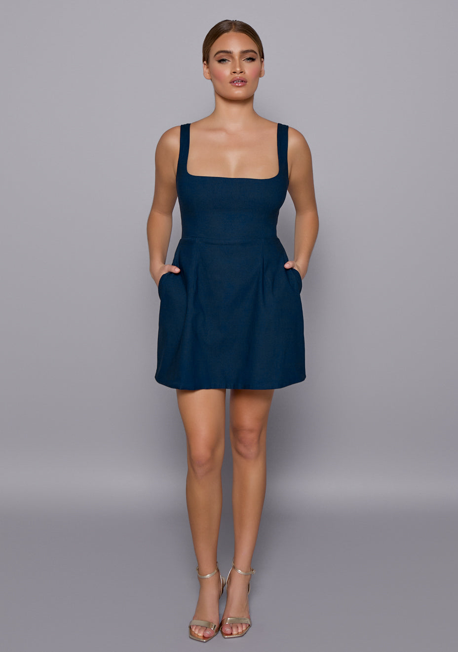 Model wearing the VSPR Camille Navy Mini Dress with a structured square neckline and wide straps, featuring a softly flared skirt, captured against a neutral studio backdrop.