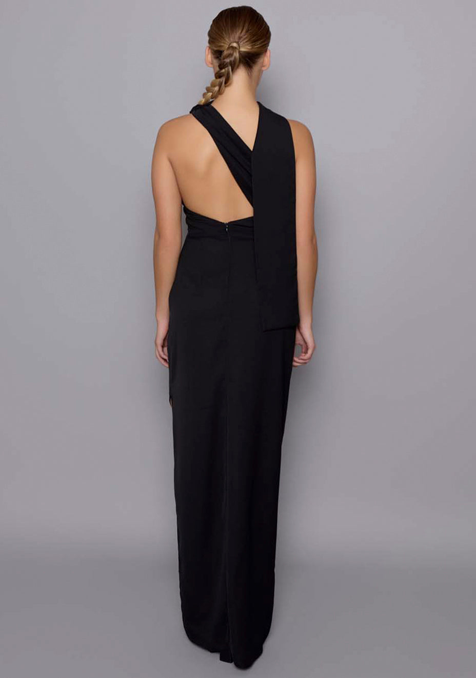 Back view of the VSPR Drew black dress revealing the asymmetric open-back cut-out and clean zip closure, with the shoulder drape cascading over one side.