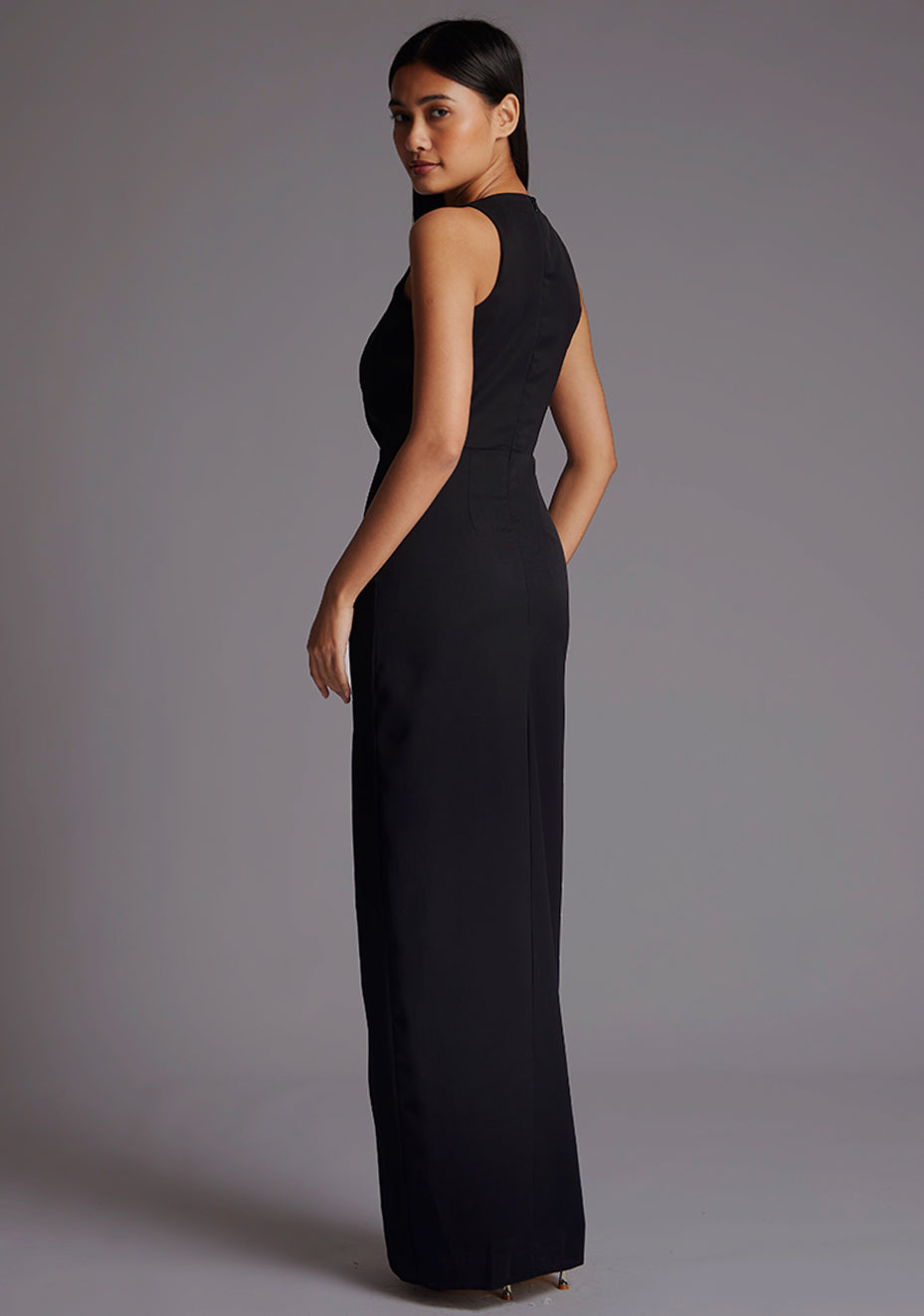 Side back image of a model wearing a black sleeveless maxi dress with sleeveless design and flattering V-neckline accentuates your figure while the body con fit gracefully hugs your curves. The design featured is the Vesper Elba V-neckline Maxi Dress in Black.