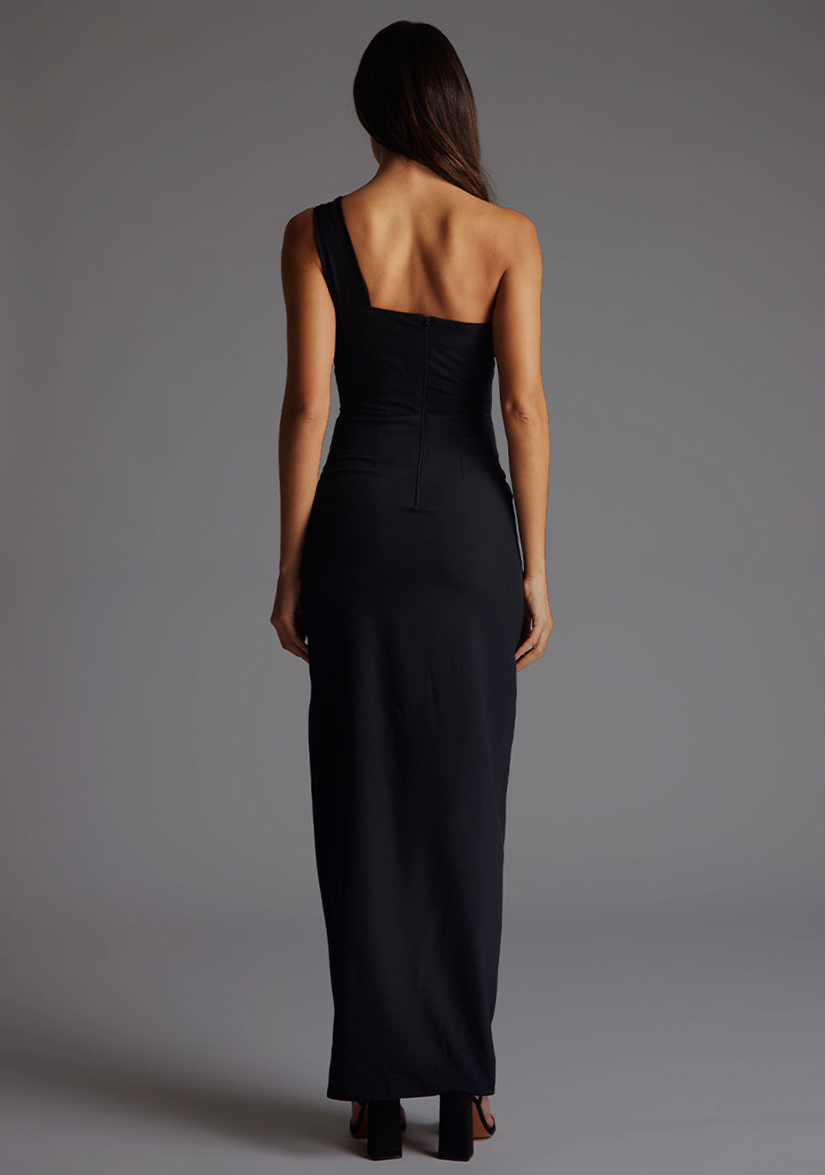 Back image of the model wearing a black maxi dress with a sleek one-shoulder silhouette, contemporary front cut-out and front skirt split for effortless chic. The design features Vesper Ellis Cut-Out One-Shoulder Maxi Dress in Black.