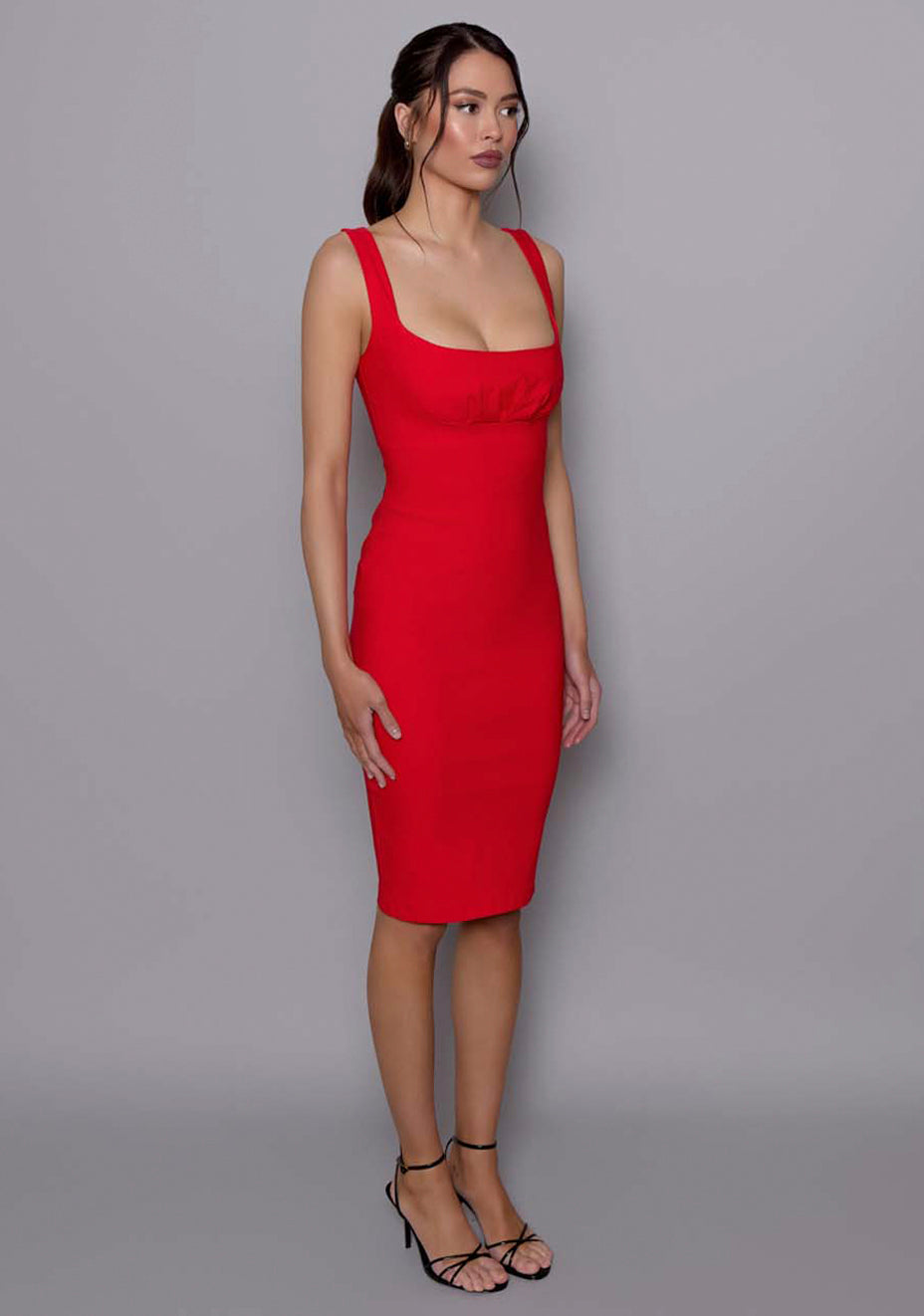 Side-front view of the VSPR Evette red dress showing the bodycon silhouette, elegant square neckline, and subtle shaping through the waist and hips.