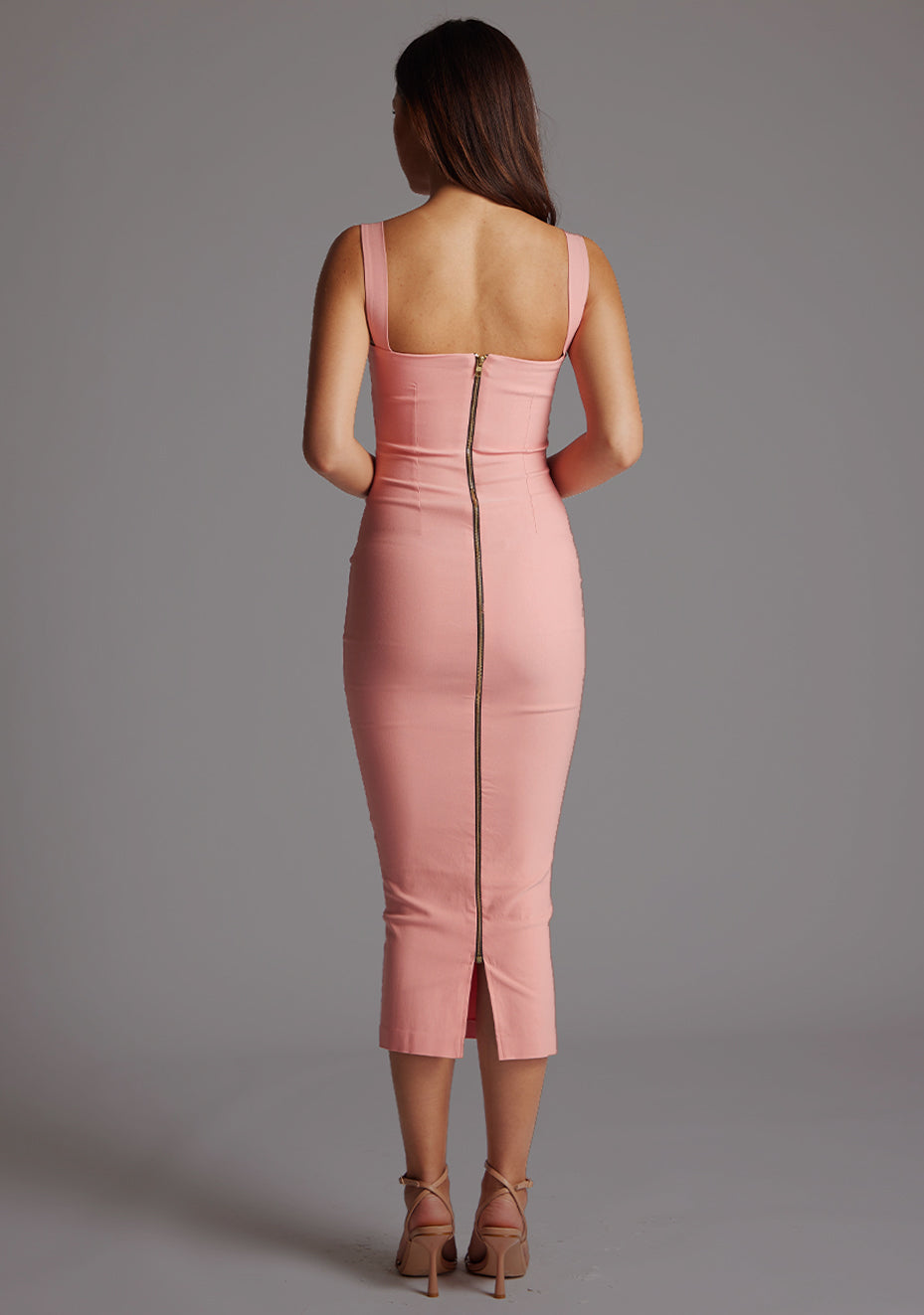 Back image of a model wearing the VSPR Frances Sweetheart Neckline Peach Midaxi Dress, highlighting its streamlined shape, centre back gold zip and graceful length on a model standing against a grey studio backdrop.