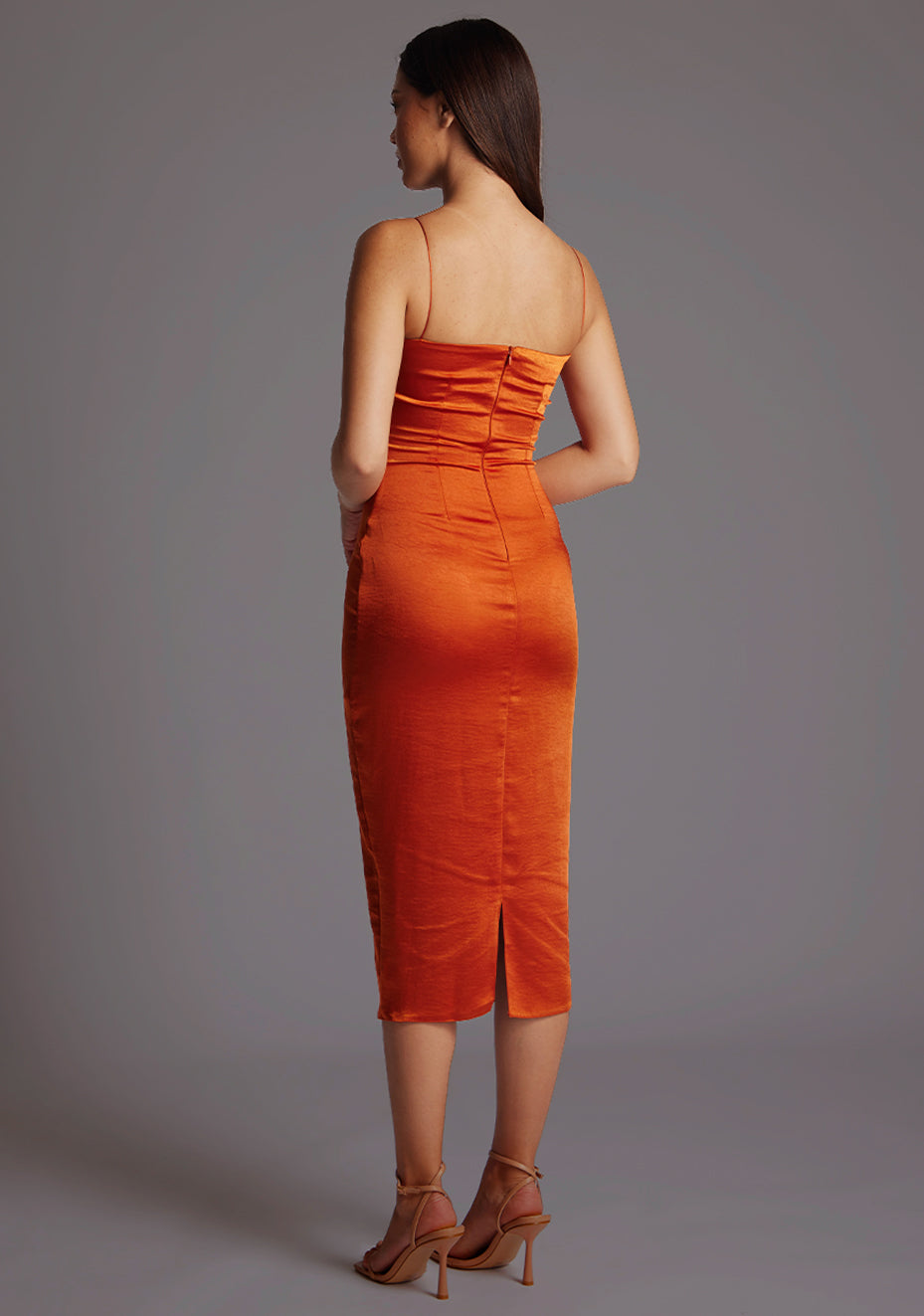 Side back image of a model wearing a rust satin dress with a timeless sweetheart neckline, delicate thin straps, and a convenient back zip. The design featured is the Vesper Hibiscus Ruched Bust Satin Midaxi Dress in Rust.