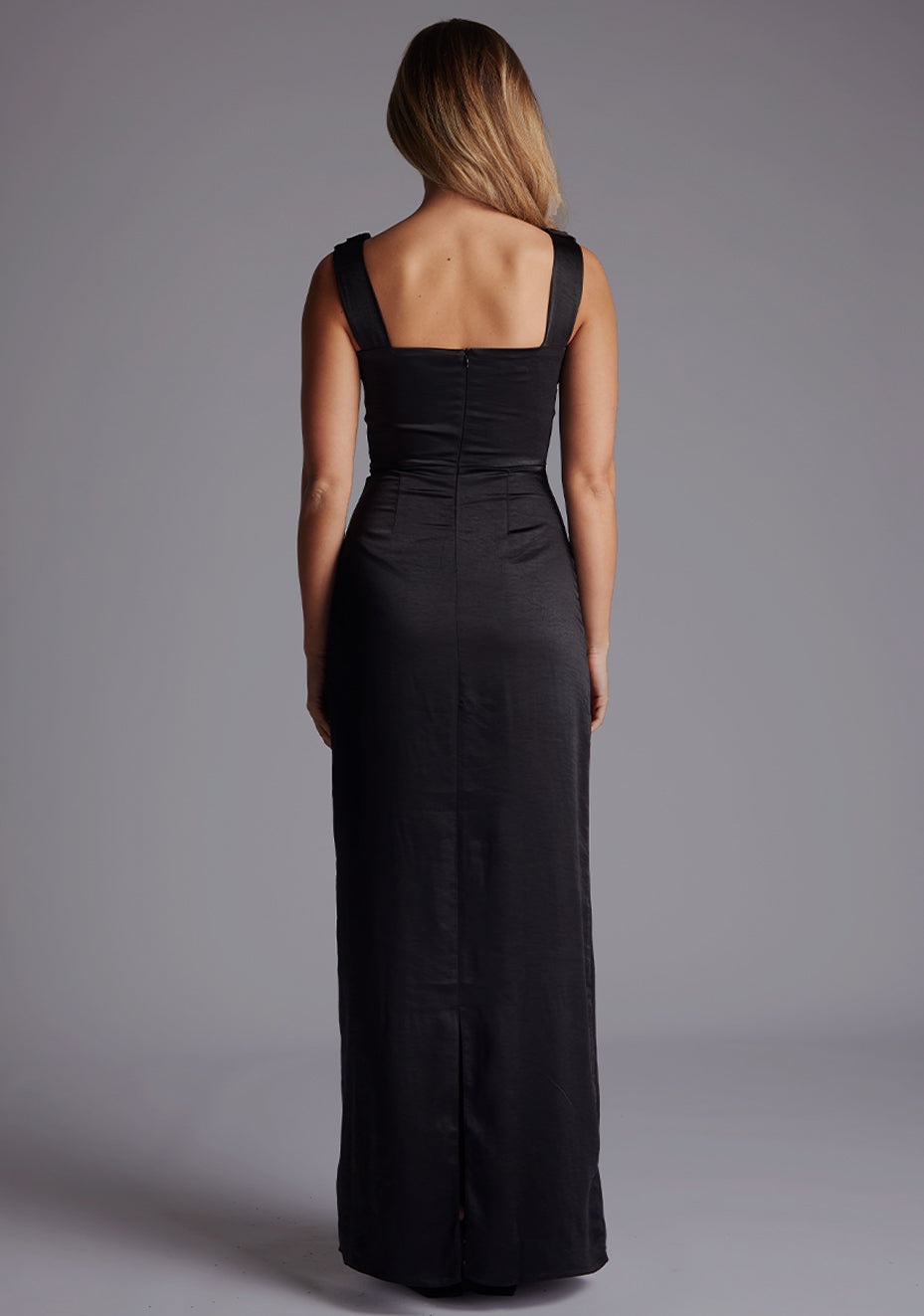 Back image of a model wearing the Vesper Jodie Cowl Neck Satin Maxi Dress in Black featuring a clean silhouette, invisible zip, and subtle skirt split.