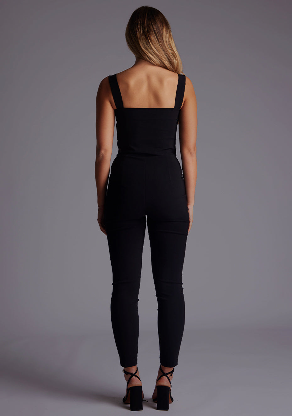 Back image of the model wearing pine green top with a sweetheart neckline and wide straps create a flattering silhouette, while the circular cut outs at the hem add a touch of edge and statement front zip. The design featured is the Vesper Juno Sweetheart Crop Top in Black with Vesper Raven High Waist Trousers in Black.