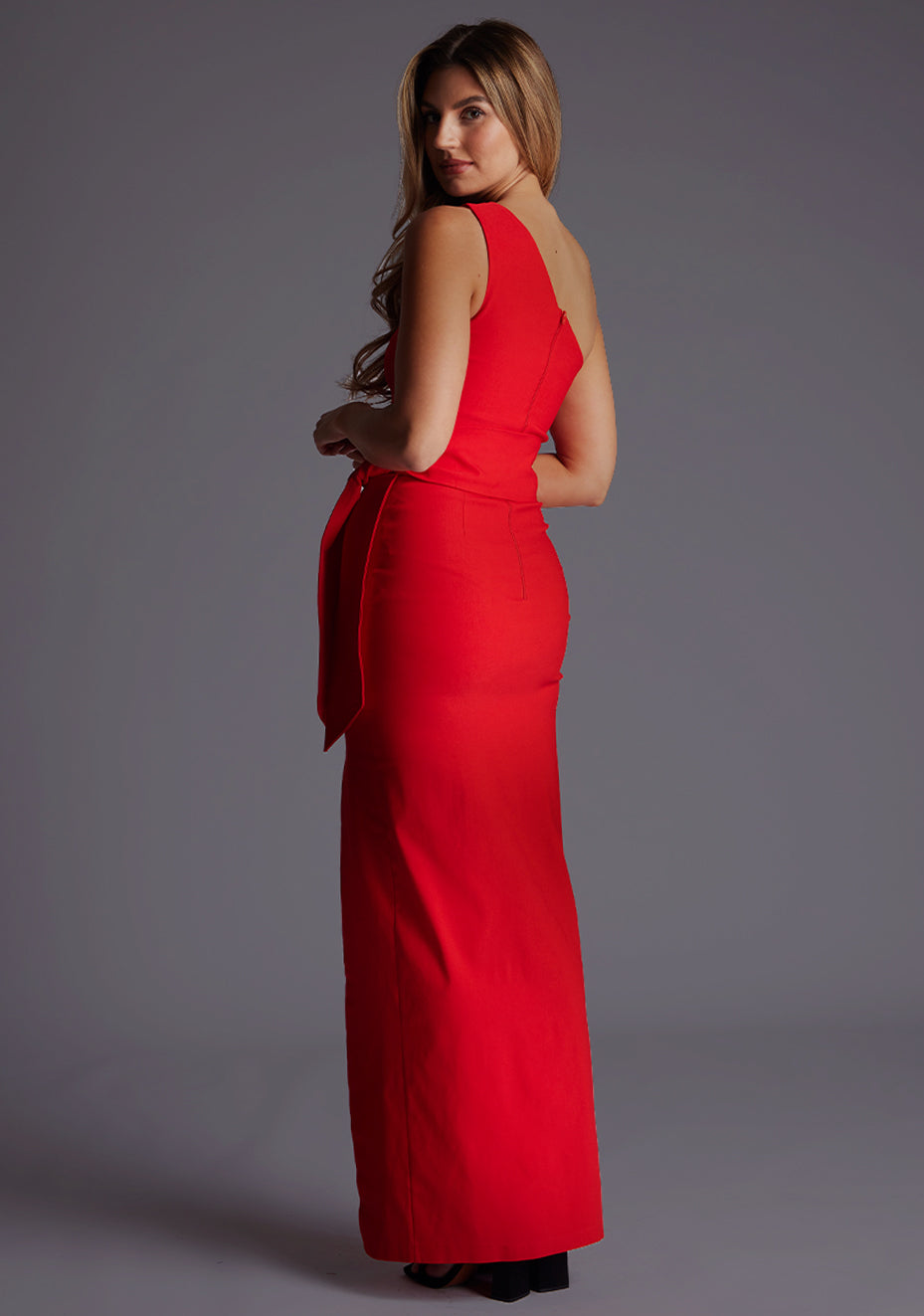 Side back image of a model wearing the Vesper Lisbeth One Shoulder Maxi Dress in Red, revealing the smooth back line and fluid maxi skirt.