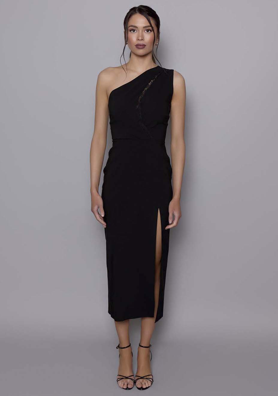 Model wearing the VSPR Madison black midaxi dress featuring a one-shoulder neckline, lace-trimmed front cut-out, and thigh-high split, standing against a neutral studio background.