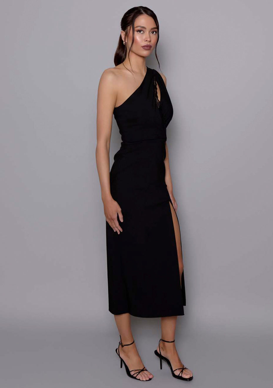 Angled side-front view of the VSPR Madison midaxi dress emphasizing the body-contouring fit, asymmetric shoulder design, and flowing front slit for a bold yet elegant silhouette.