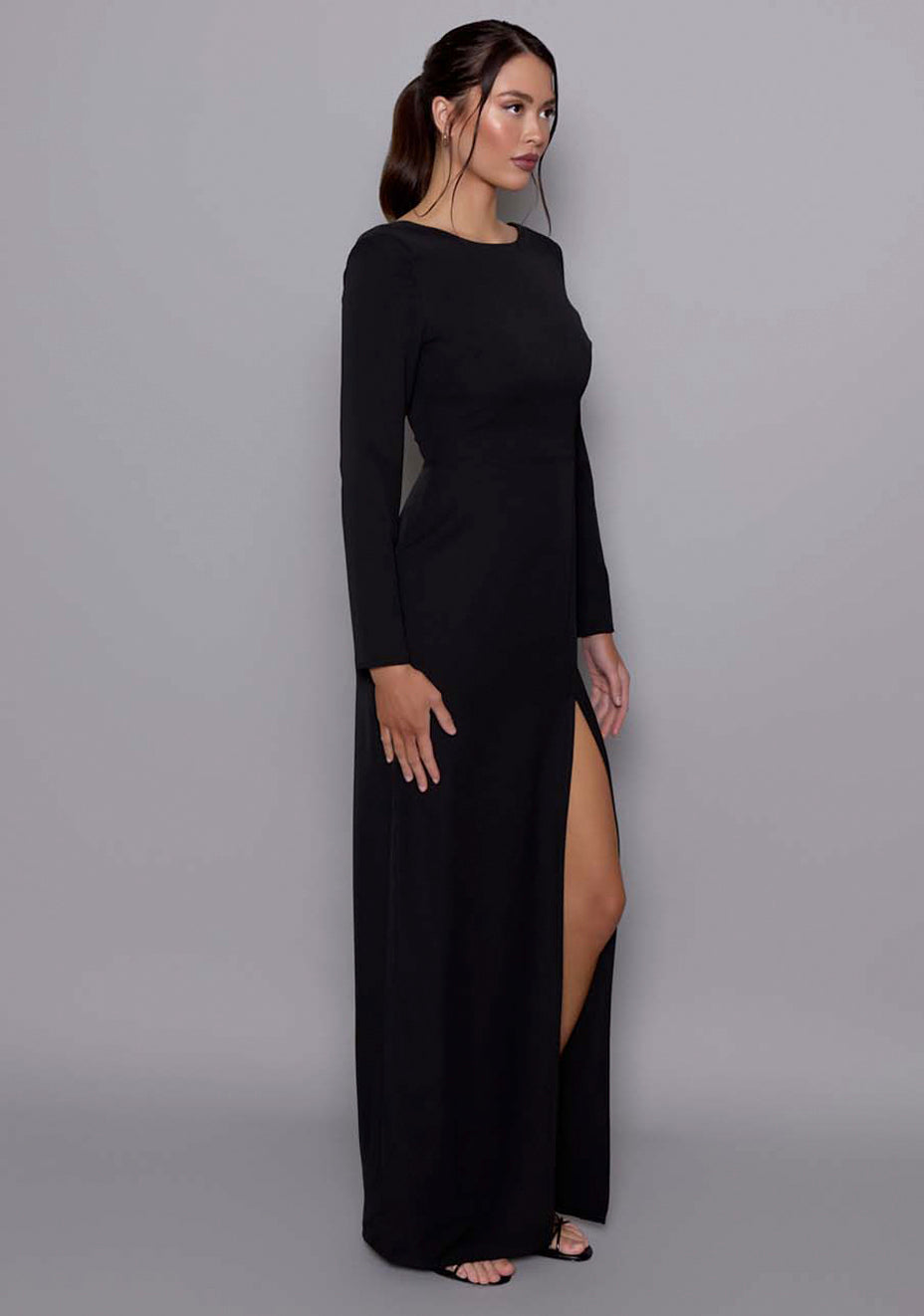 Side front view of the VSPR Mandy Black maxi Dress showcasing the long sleeves, scoop back, and front skirt split for a sophisticated yet alluring look.