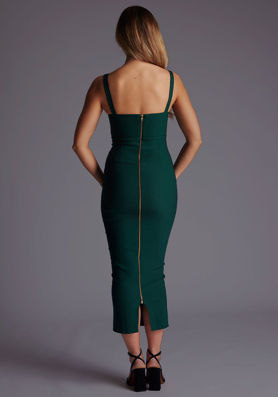 Back image of a blonde model wearing a Forest Green Midaxi Dress with a flattering scoop neckline that accentuates the collarbone and a bodycon silhouette that effortlessly enhances your curves. The design features is the Vesper Marleen Scoop Neck Bodycon Midaxi Dress in Forest Green.