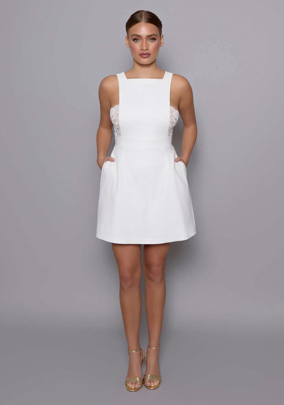 Model wearing the VSPR Noa Open Back Mini Dress in Ivory with a squared neckline, wide straps, and fluid A-line skirt, standing against a gray studio backdrop.