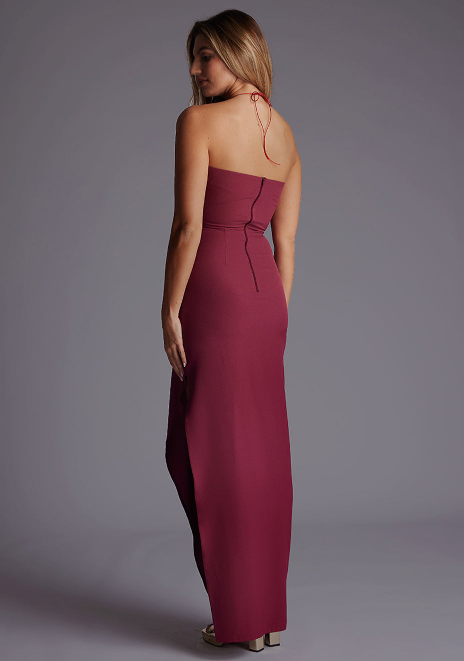 Side back image of a model wearing the Vesper Opal Cut-Out Halter Maxi Dress in Burgundy, revealing the sleek back line and flowing maxi skirt.