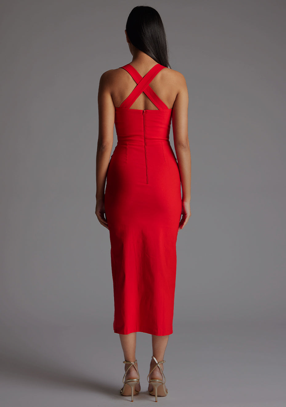 Back image of a model wearing a red midaxi dress, featuring plunge sweetheart halter neck straps which cross at the back and a front skirt split. The dress featured is the Vesper Poppy Red Sweetheart Midaxi Dress