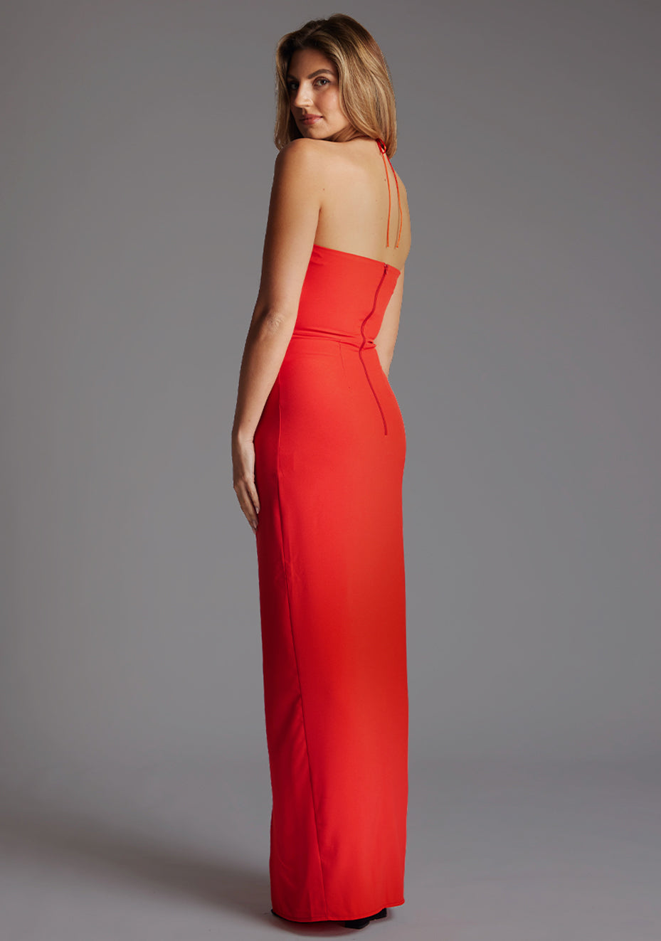 Side back image of a model wearing the Vesper Sadie Halter Neck Maxi Dress in Red, revealing the daring low back and elegant halter tie.