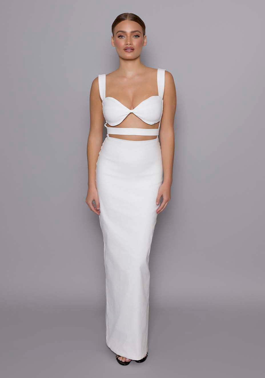 Model wearing the VSPR Solene ivory cut-out maxi dress featuring a structured sweetheart neckline, under-bust cut-outs, and wide supportive straps, standing against a gray studio backdrop.