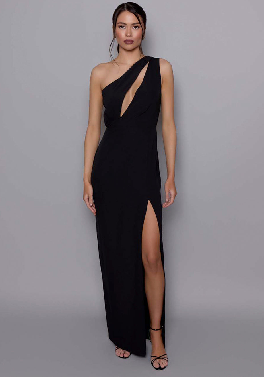 Model wearing the VSPR Vanessa black one-shoulder maxi dress with front cut-out and ruched waist shaping, featuring an elegant draped shoulder panel, set against a grey studio background.