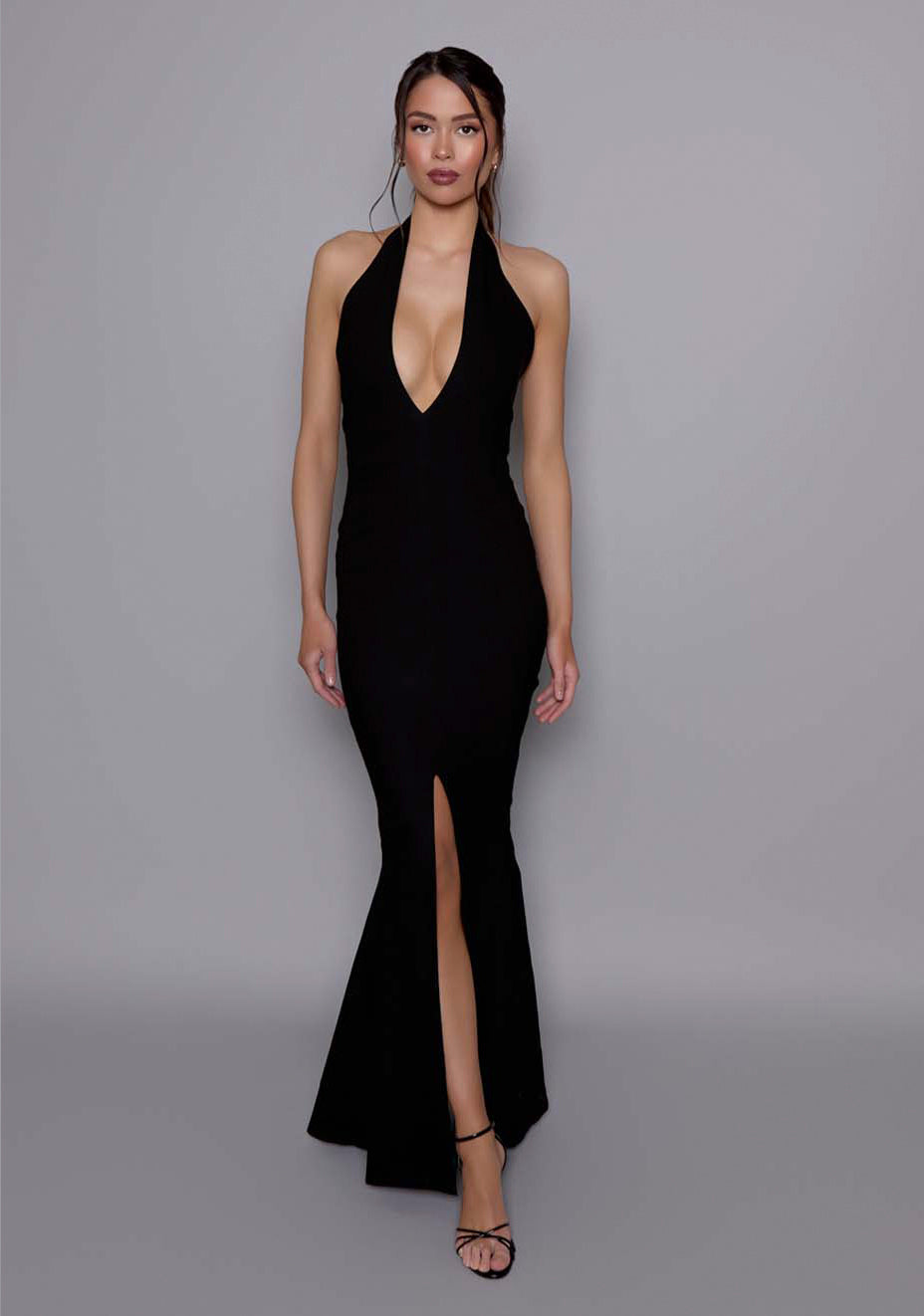 Model wearing the VSPR Zara black fishtail maxi dress with a plunging halter neckline, darted bodice, and flowing skirt, standing against a gray studio backdrop.
