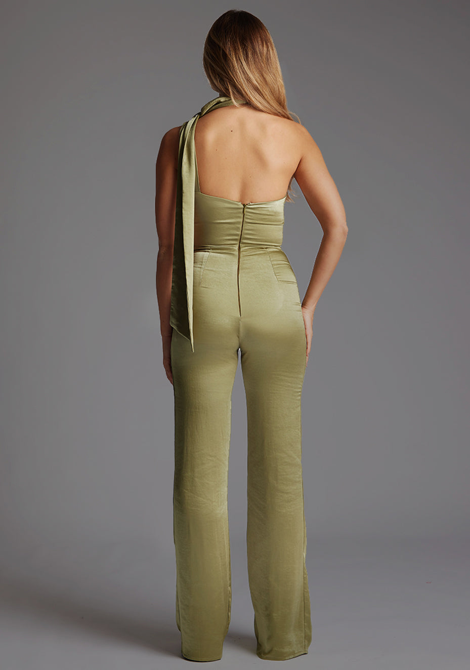 Back image of a model wearing a olive collar detail jumpsuit with asymmetric one-shoulder design and a unique collar detail and wide leg that adds sophistication. The design featured is the Vesper Kaitlin Olive Collar Detail Jumpsuit.