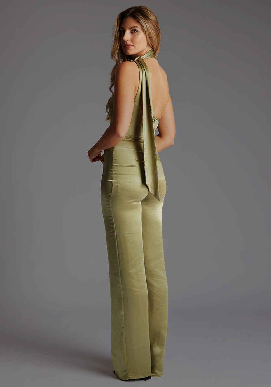 Back quarter image of a model wearing a olive collar detail jumpsuit with asymmetric one-shoulder design and a unique collar detail and wide leg that adds sophistication. The design featured is the Vesper Kaitlin Olive Collar Detail Jumpsuit.