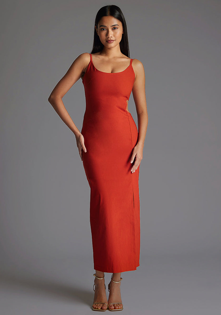 Front image of the model wearing a rust midaxi dress with a scoop neckline, bodycon silhouette, side cut out and front skirt split . The design featured is the Vesper Maryam Rust Midaxi Dress.