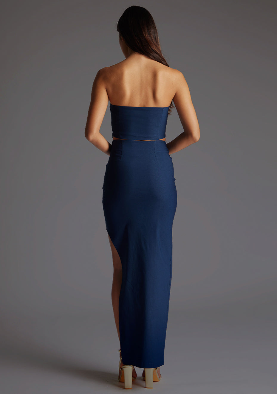 Back image of the model wearing a navy skirt with a stunning skirt features a stylish side split that adds a touch of allure to your ensemble. The design featured is the Vesper Monot Navy Skirt pair with Vesper Benedetta Navy Top