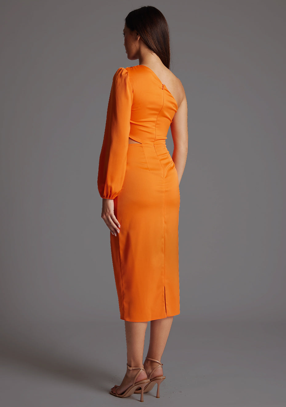 Back quarter image of a model wearing an orange mid dress with a asymmetric, one long sleeve design and subtle side cut-out. The design featured is the Vesper Niccola Orange Midi Dress