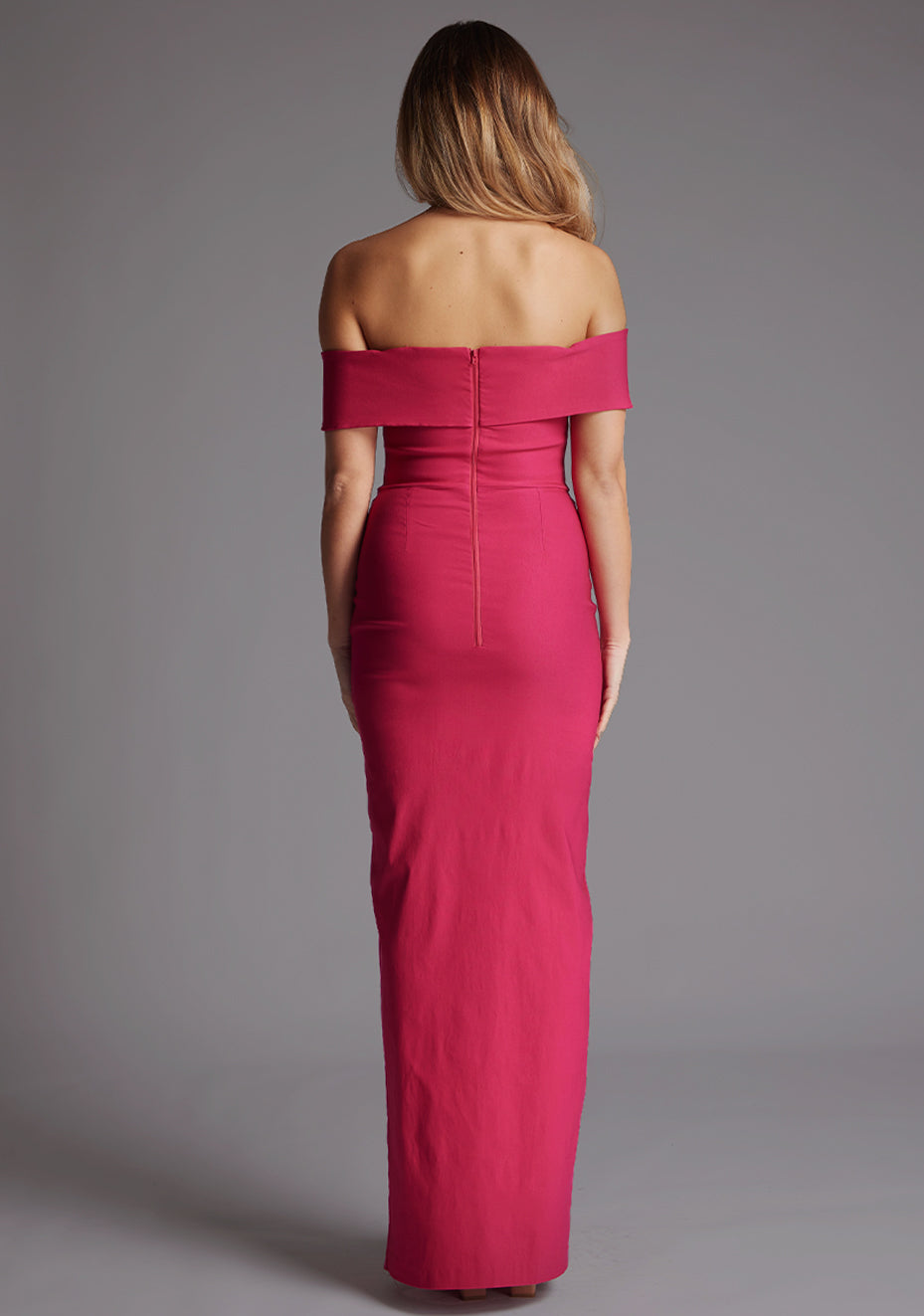 Back image of a model wearing a cerise maxi dress with a sweetheart neckline with curved band detail at bust, beck line at top of arms and finished with a front skirt split. The design featured is the Vesper Ivory Cerise Maxi Dress
