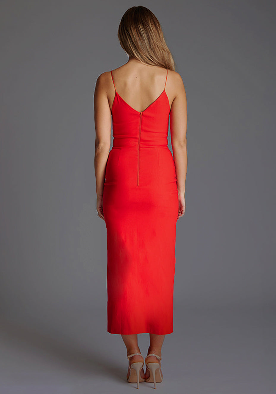 Back image of blonde model wearing a red midaxi dress with a plunge neckline, delicate thin straps for a feminine touch, and front split that adds a modern edge. The design featured is the Vesper Palmer Red Midaxi Dress.