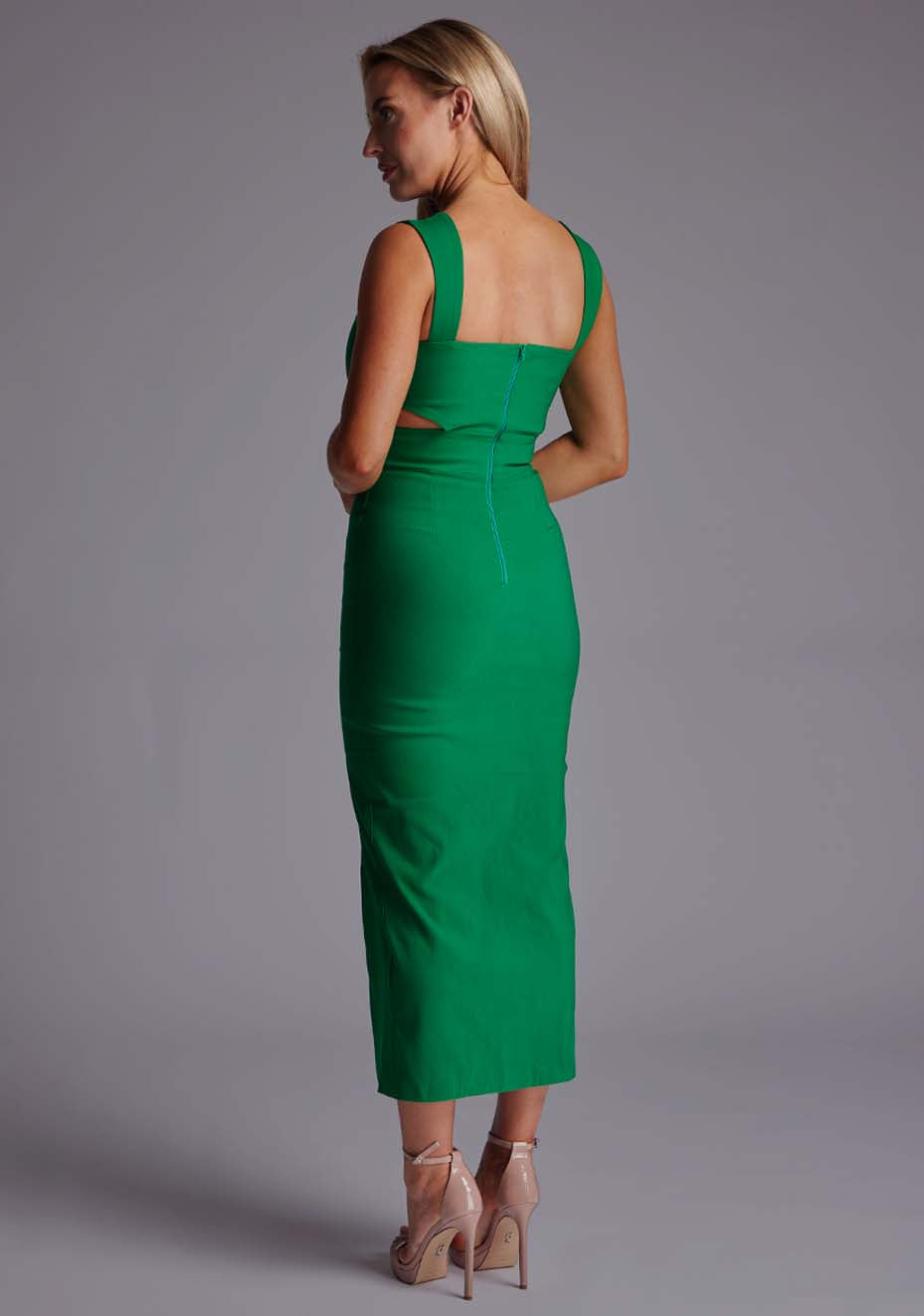 Back quarter image of a model wearing a green cut out midaxi dress with a sweetheart neckline with wide straps, a side cut-out and front skirt split. The design featured is the Vesper Porticini Emerald Green Cut Out Midaxi Dress