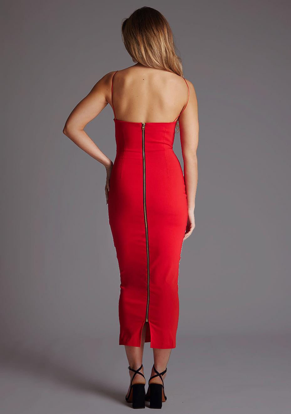 Back image of a model wearing a red midaxi dress with a scoop neckline, thin straps, a bodycon fit and centre back invisible zip and small keyhole cut-out at bust. The design featured is the Vesper Roxanne Red Midaxi Dress.