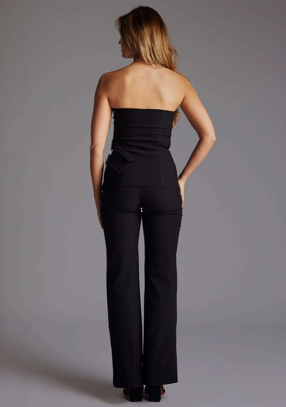 Back image of a model wearing a strapless black to with a chic strapless design with modern buckle detail. The design featured is the Vesper Sharon black Top paired with the Vesper June Black Wide Leg Trousers