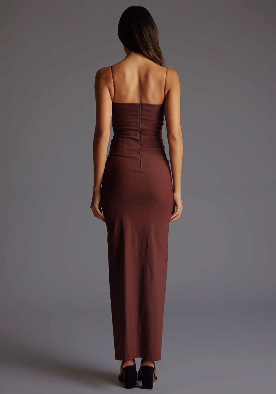 Back image of a model wearing a chocolate maxi dress with a chic square neckline with an elegant cutout, complemented by delicate thin straps, back zip ensures a seamless fit and a front skirt split. The design featurd is the Vesper Suki Chocolate Maxi Dress.