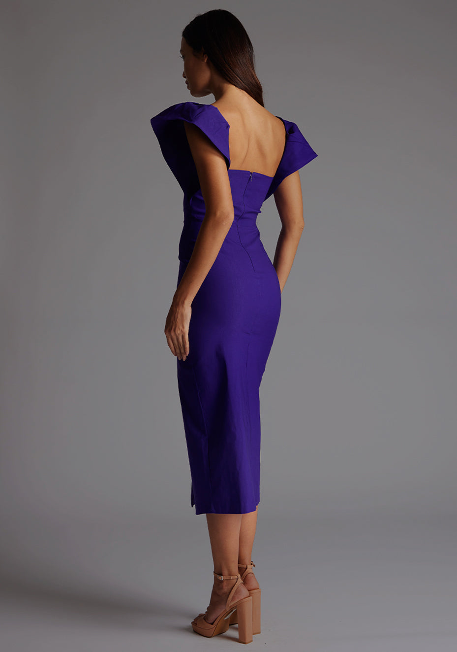 Back quarter image of model wearing a purple frill sleeve midaxi Dress with a sweetheart neckline, short frill hem cap sleeves and a front skirt split. The design featured is the Vesper Sunday Purple Frill Sleeve Midaxi Dress.