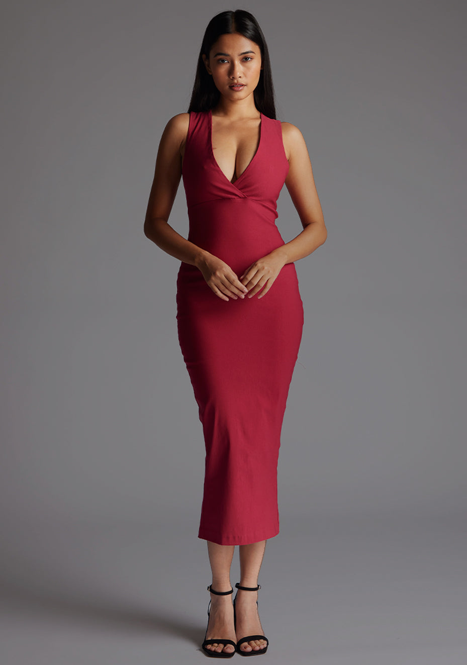 Front image of a model wearing a raspberry midaxi dress with a stunning sleeveless masterpiece, plunging v-neckline ,slim silhouette and cross back and gold zip at the back. The design featured is the Vesper Verona Raspberry Midaxi Dress