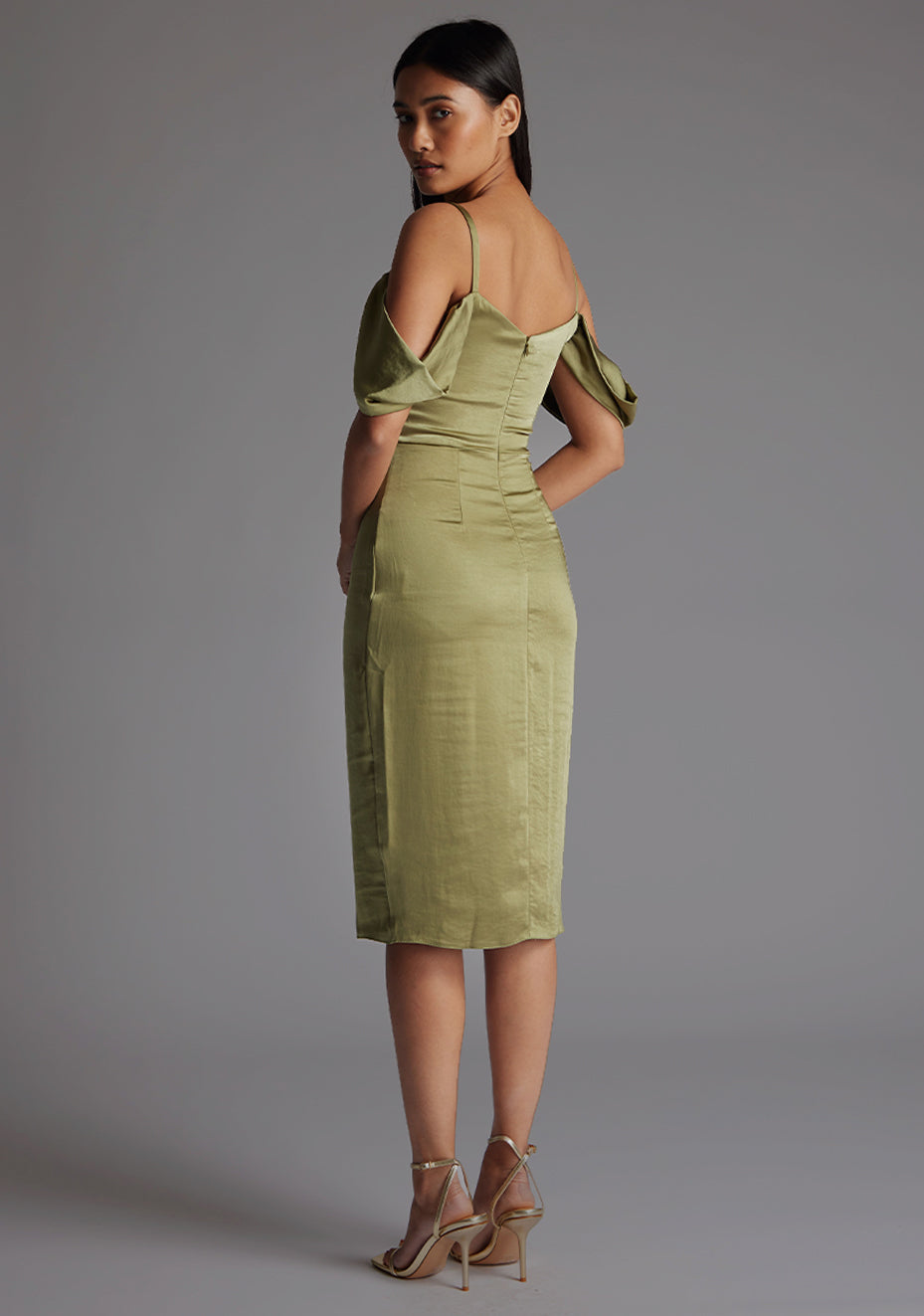 Back quarter image of model wearing a olive satin bardot midi dress with a delicate allure satin, cowl neckline and invisible back zip with thin straps and draped arm bands. The design featured is the Vesper Victoria Olive Satin Bardot Midi Dress