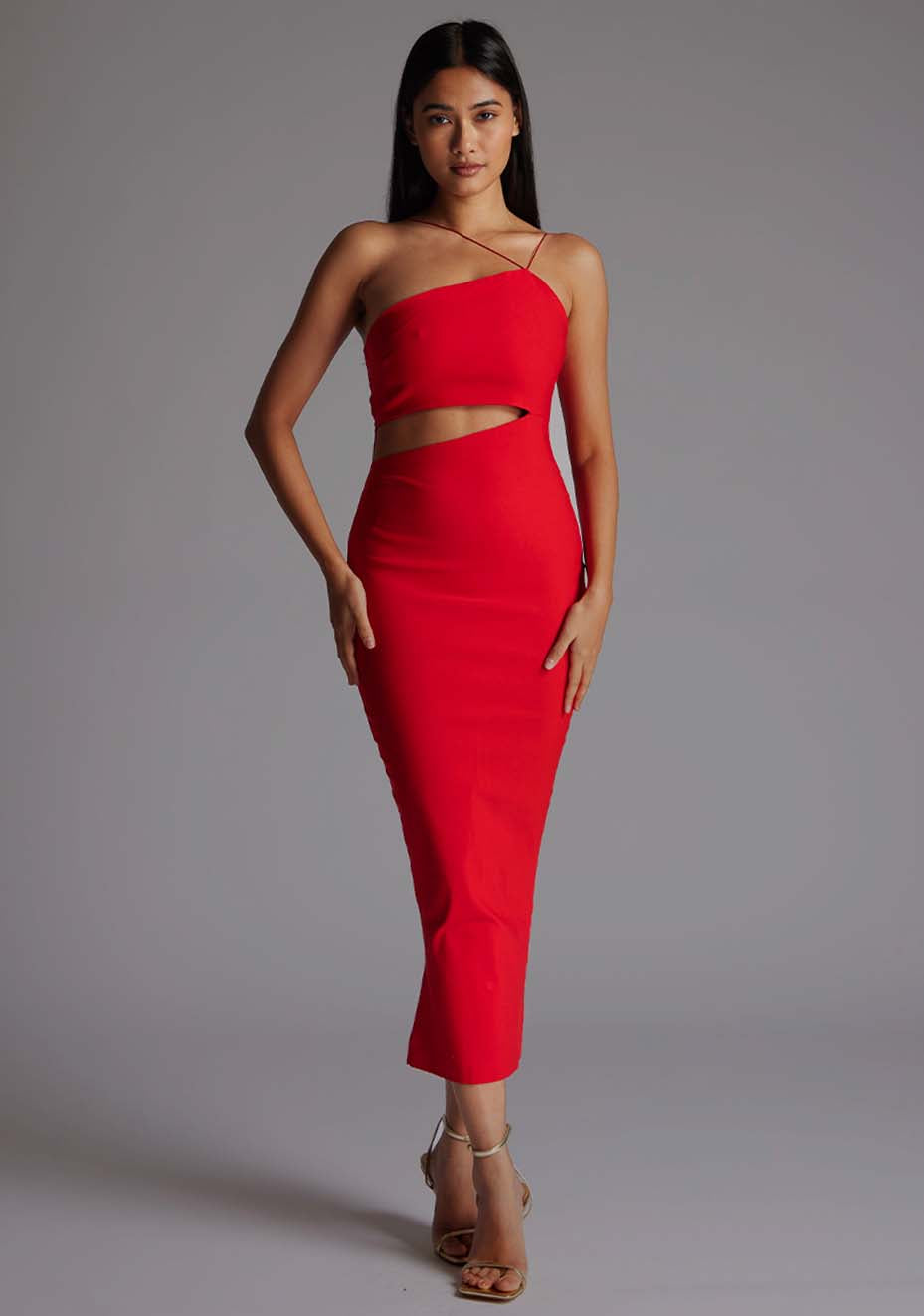 Front image of a model wearing a red midaxi dress with a asymmetric neckline and one shoulder with double thin strap detail on shoulder and across chest create a unique and elegant design, while the side waist cut-out and centre back gold zip add an extra touch of glamour. The design featured is Vesper Whitney Red Midaxi Dress