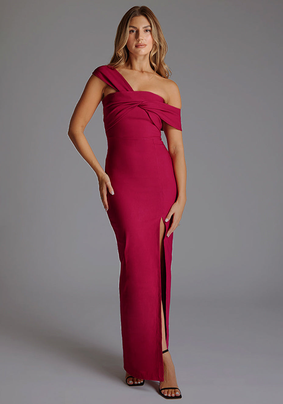 Front image of blonde model wearing a Raspberry Maxi Dress with a asymmetrical silhouette, front skirt split and a bodycon fit. The design features is the Vesper Winslow Raspberry Maxi Dress